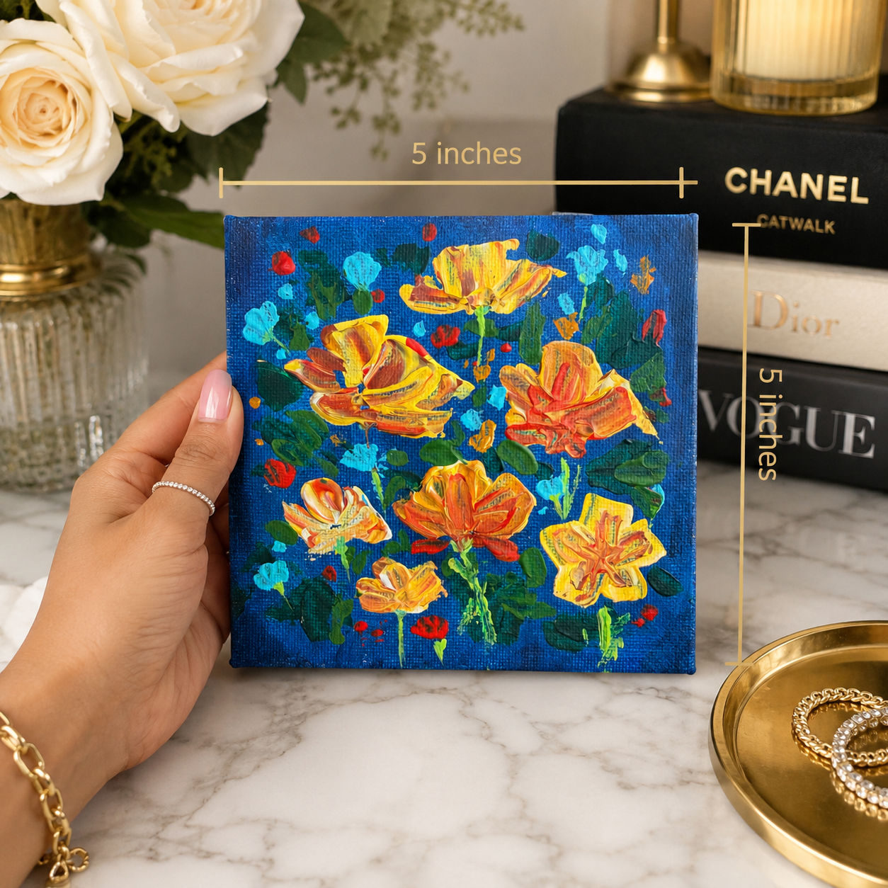 Hand holding a small floral painting with books and flowers in the background