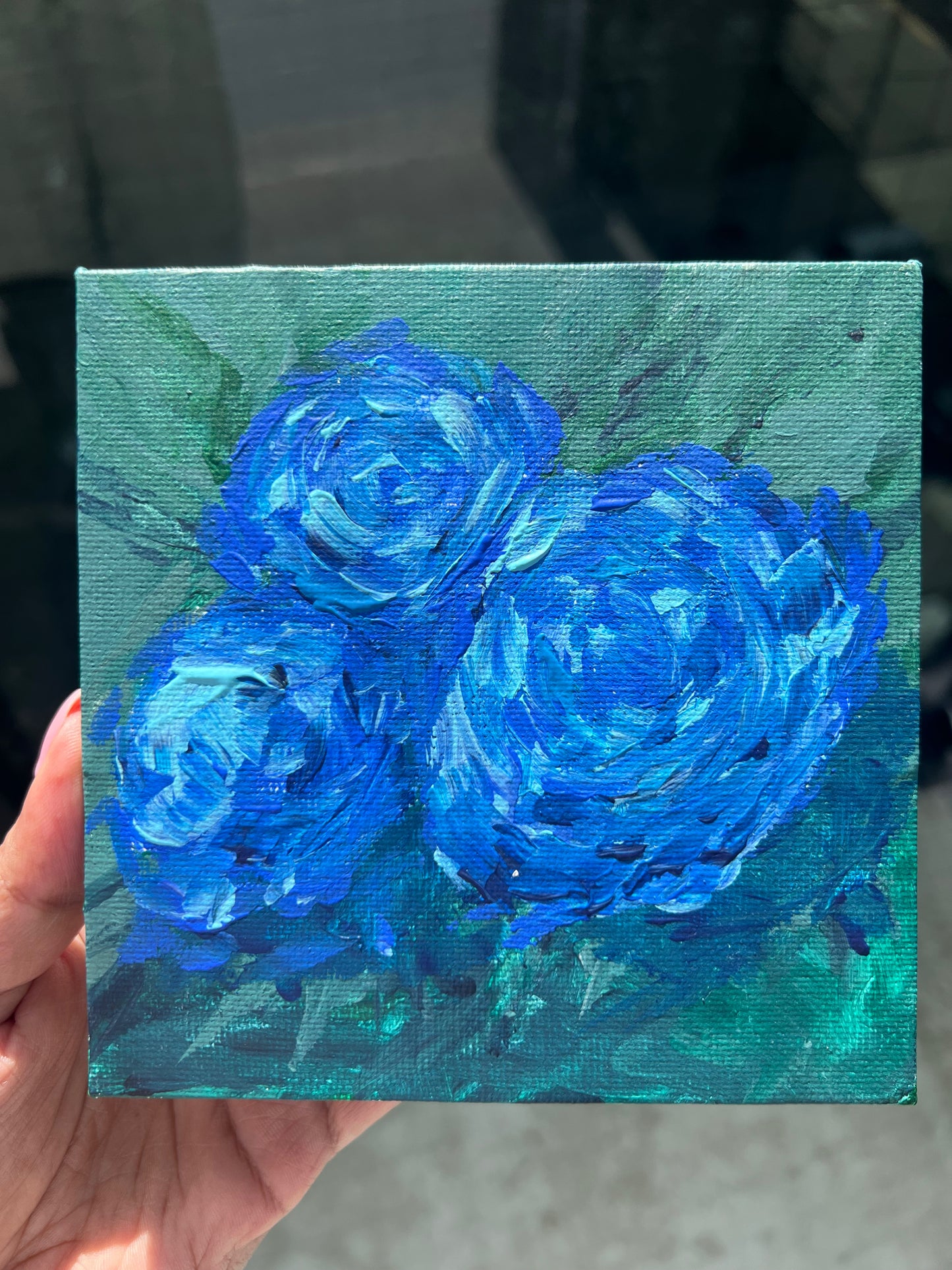 Small canvas painting of blue roses held by a hand.


