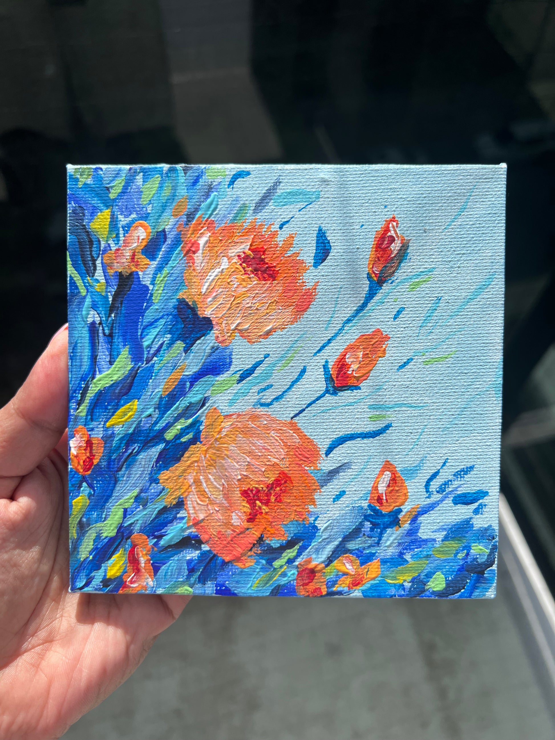Hand holding a small painting of orange flowers on a blue background

