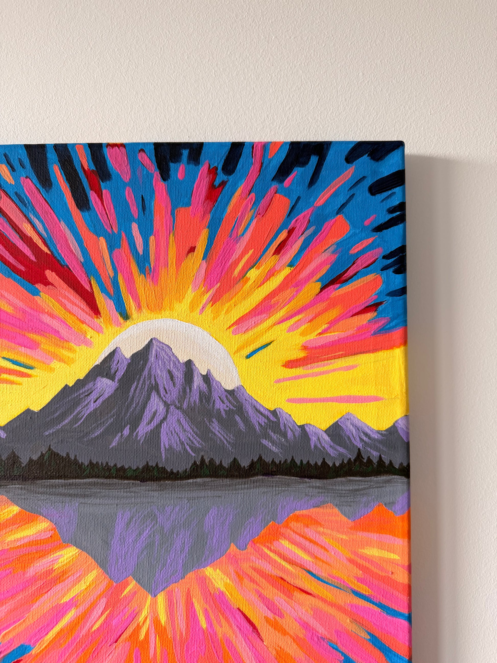 Canvas painting of a mountain with a colorful sunburst on a white wall