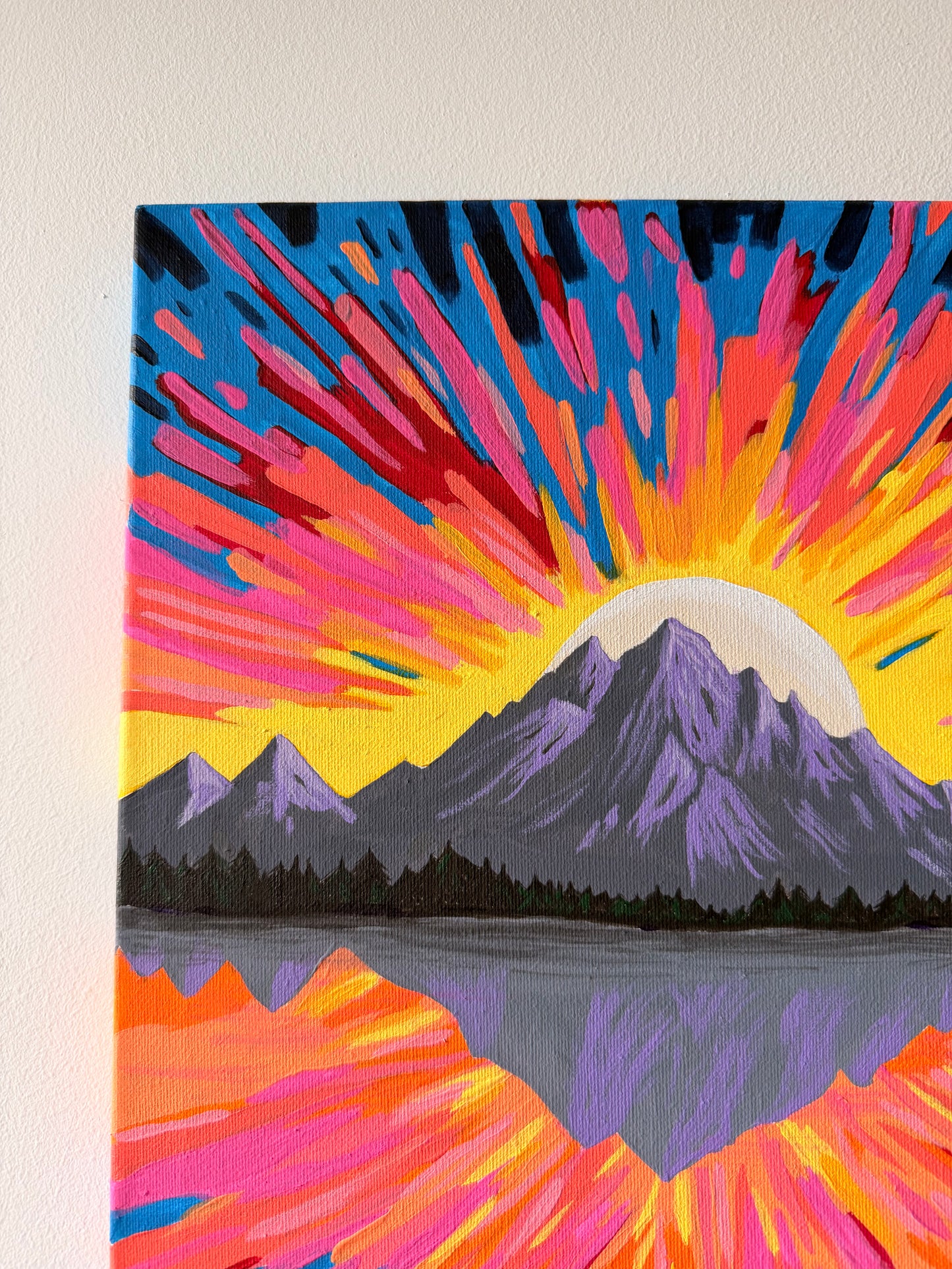 Colorful abstract painting of mountains and a sun on a beige wall.